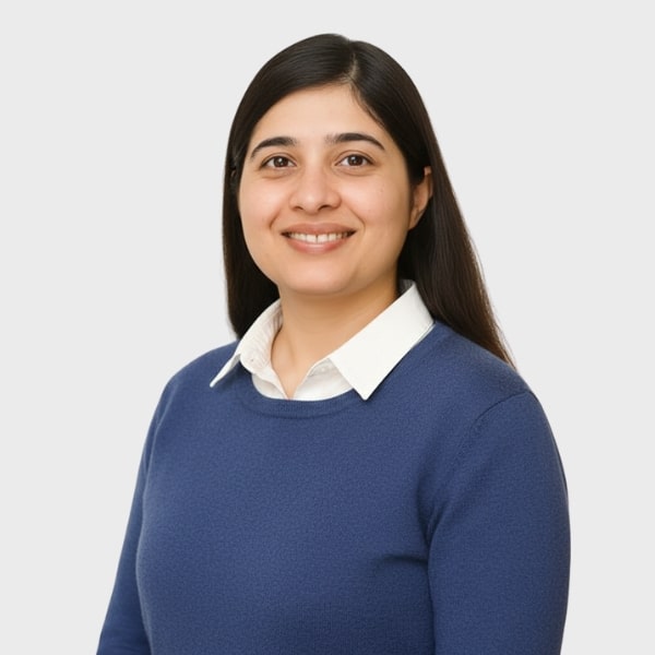 A woman with long dark hair, wearing a white collared shirt under a blue sweater, is smiling and facing the camera against a plain light gray background, reflecting the professional image of an IT staffing agency in Toronto.