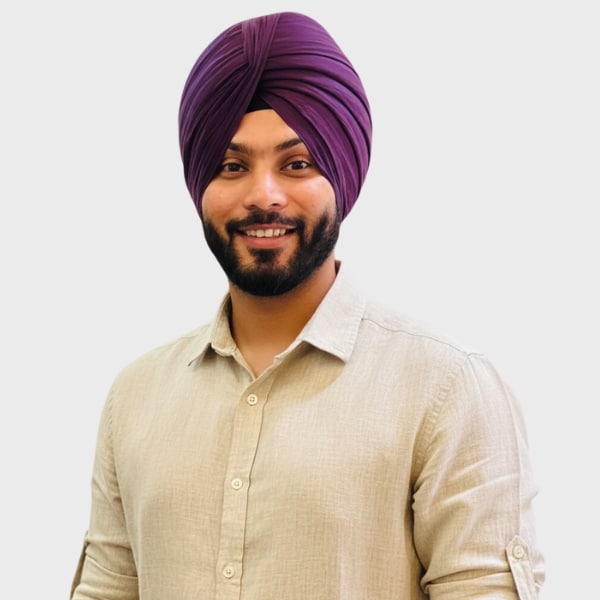 A smiling man with a beard, wearing a purple turban and a light beige button-up shirt, poses confidently against a plain background—perfect for showcasing the diverse talent represented by an IT staffing agency in Toronto.
